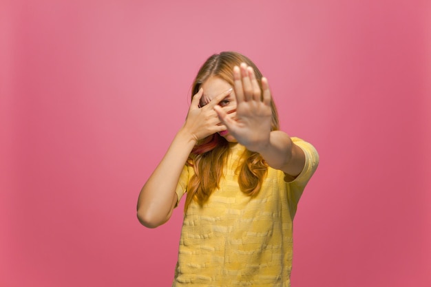 Bang, beschaamd jong meisje dat ogen bedekt met een stopgebaar, wil niet kijken in roze studio