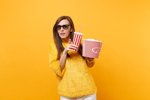 Bang jonge vrouw in 3d imax bril wijzende wijsvinger, kijken naar film film houden emmer popcorn kopje cola of frisdrank geïsoleerd op gele achtergrond. Mensen oprechte emoties in de bioscoop, levensstijl.
