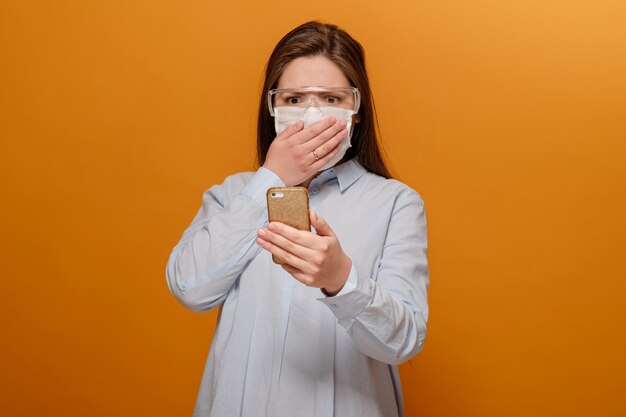 Bang jonge vrouw met een medisch masker op haar gezicht kijkt naar de telefoon, vrouw in paniek over epidemie