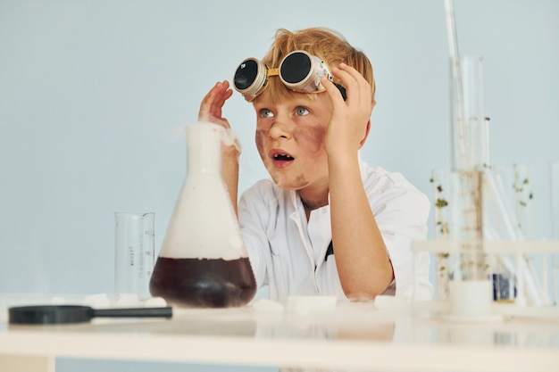 Bang jongetje in jas die een wetenschapper in het lab speelt met behulp van apparatuur