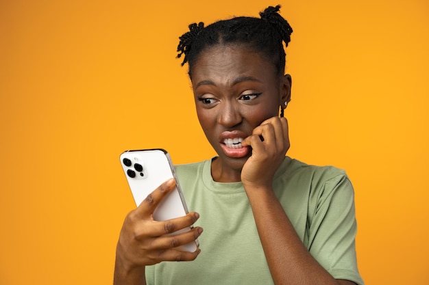 Bange Afro-Amerikaanse vrouw met mobiele telefoon die slecht nieuws ziet tegen gele achtergrond