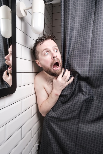 Bange bebaarde man gluurt achter het gordijn in de douche hij is geschokt