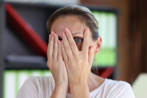 Bange vrouw bedekt haar gezicht met haar handen en kijkt door haar vingers naar camera close-up