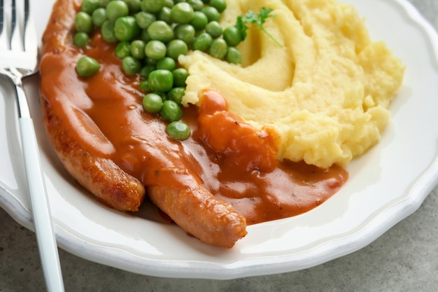 Bangers en puree Gegrilde worstjes met aardappelpuree en groene erwt op witte plaat op grijze achtergrond Traditioneel gerecht van Groot-Brittannië en Ierland BBQ-rundvleesworstjes Bovenaanzicht