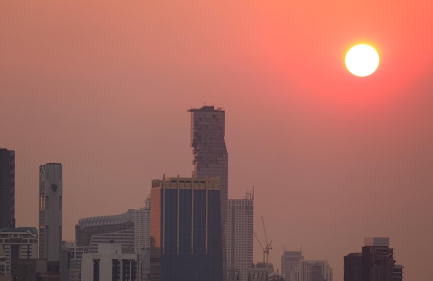 グラデーションのオレンジ色の空に輝く明るい太陽とバンコク市のスカイライン