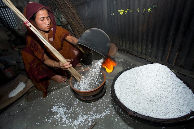 Bangladesh 09 februari 2018 Een bejaarde dorpsvrouw bereidt khoi gepofte rijst van Binni Dhan kaf kleefrijst als Bengalis traditionele festivals maaltijden in savar Dhaka