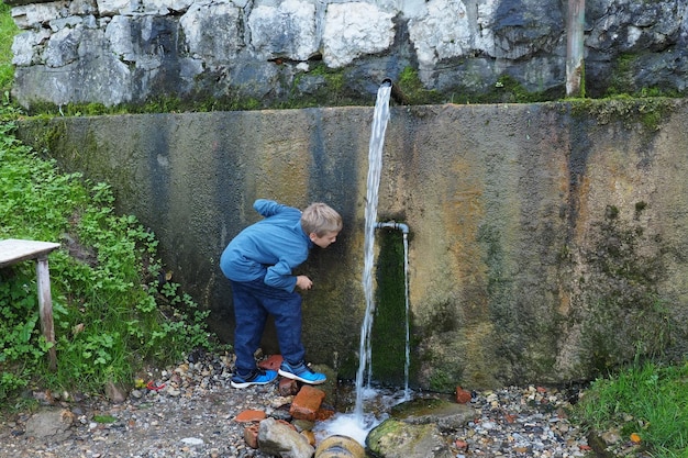 Banja Koviljaca Loznica Serbia Mount Guchevo park and forest Source of mineral sulfuric and ferruginous water Ilidja Chesma Cesma A jet of water pours out of a tap in a concrete wall A boy