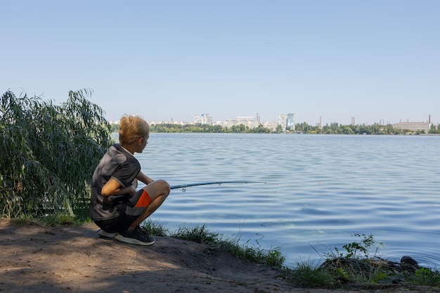 On the bank of a river a boy is fishing while watching a float Sport fishing on the river in summer