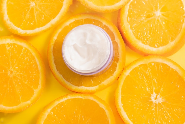 Bank of white moisturizing thick cream for face and body on a background of oranges. Natural vitamin C product for anti-age effect.