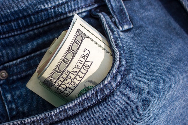 Bankbiljetten van honderden Amerikaanse dollars worden in een buis gedraaid en steken uit een spijkerbroekzak