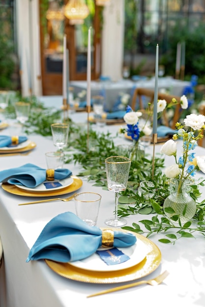 Banket bruiloft tafel setting met blauwe servetten, gouden bestek, kristal, verse bloemen en kaarsen. Bruiloft decoraties. Zachte selectieve focus.