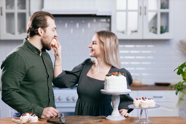 Banketbakker, banketbakker, jonge blanke vrouw met echtgenoot, vriend, man, probeer de smaak van cake op de keukentafel Taarten, cupcakes en zoet dessert