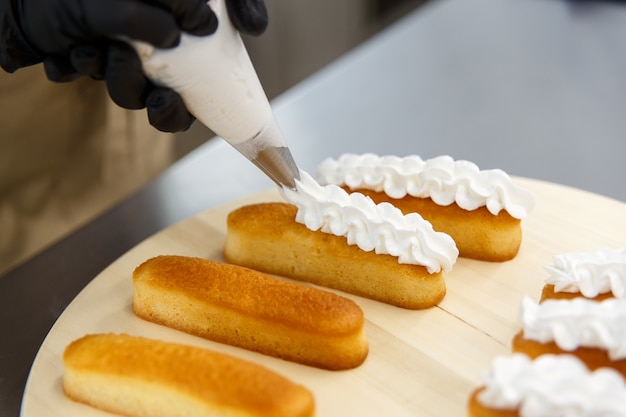 Banketbakker brengt de room op de cake, koekjescake aan met behulp van een spuitzak. Cake maken proces.