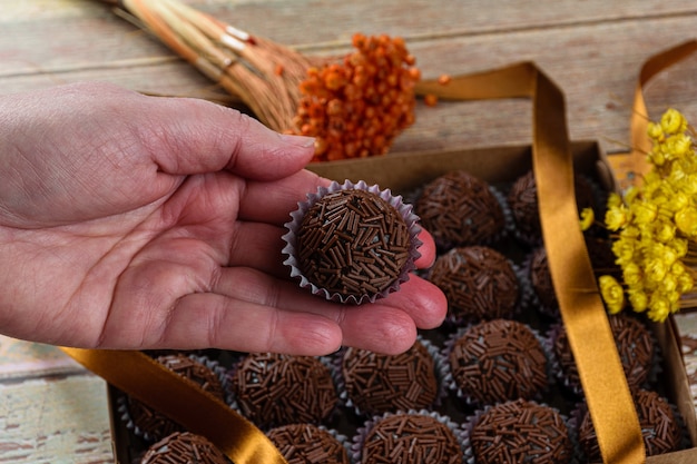 Foto banketbakker die een brigadeiro houdt. op de achtergrond een doos met verschillende brigadeiros naast een striklint.