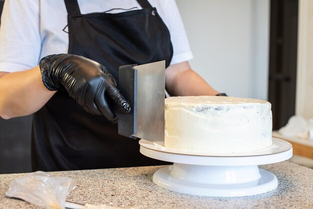 Banketbakker kok banketbakker of bakker in zwarte handschoenen en zwarte keukenschort maakt een taart. Zelfgemaakte verjaardagstaart. Concept van zelfgemaakt gebak, taarten koken, hobby. Vrouwelijke kleine bedrijf aan huis.