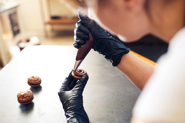 Banketbakker perst chocoladeroom uit een spuitzak op koekjes en maakt sandwich met chocoladekoekjes