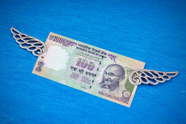 Photo banknote 100 indian rupees with decorative silver wings on a blue background