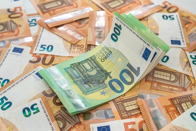 Banknotes of 50 euros are laid out and on them are banknotes of 100 euros on the table