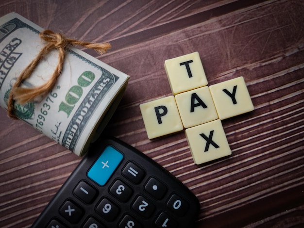 Banknotes and calculator with the word TAX PAY or PAY TAX on wooden background