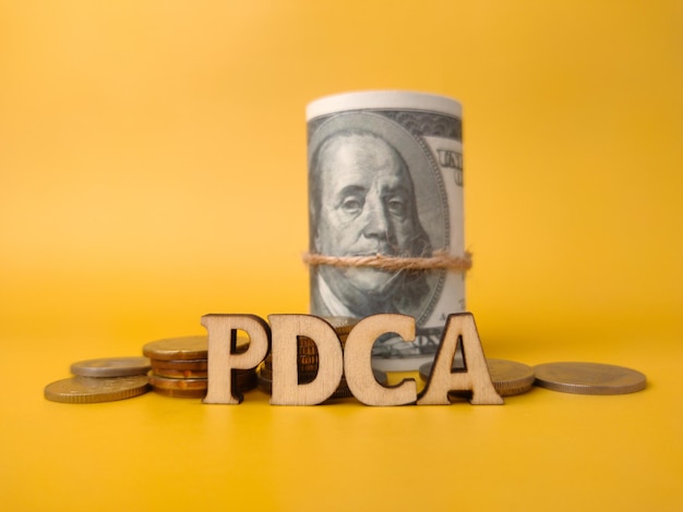 黄色の背景に単語 PDCA と紙幣と硬貨