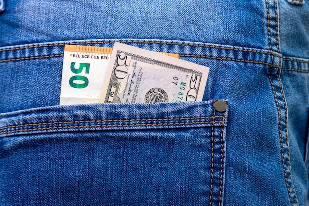 Banknotes in denominations of 50 euros and dollars in blue jeans back pocket close-up.