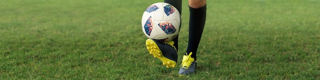 Photo banner 1x4 with the feet of a young football player in boots and with a ball on the football field