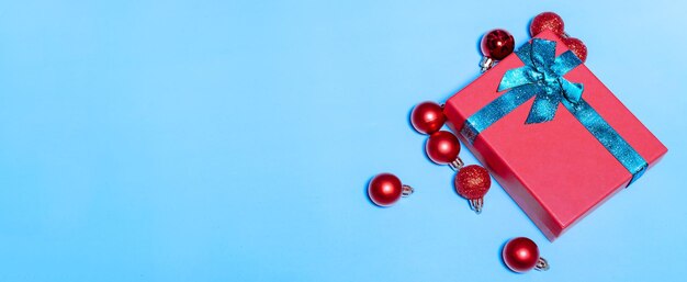 Banner of Beautiful Christmas red balls and a red gift with a green ribbon decorating toys on a blue background New year christmas concept Flat lay festive mockup with copy space