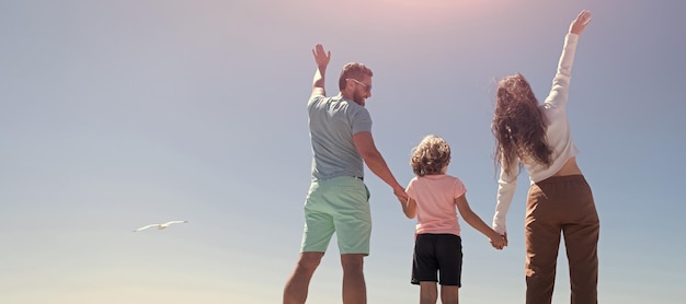 Banner of family embracing on sea beach summer family vacation\
horizontal banner family of mother father and kid boy looking in\
future holding hands in summer back view