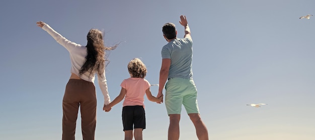 Banner of family embracing on sea beach summer family vacation\
horizontal banner mother father and child son looking in future\
holding hands in summer back view charity