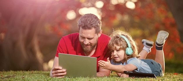 Banner of father on son school boy with laptop study online lying on grass happy family of father and son use laptop for video call in park family day