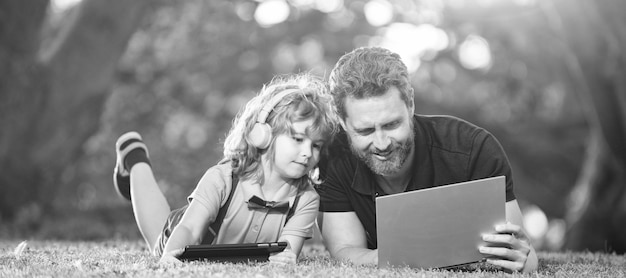 Banner of father on son school boy with laptop study online lying on grass online education on laptop father and son use modern communication technology in park