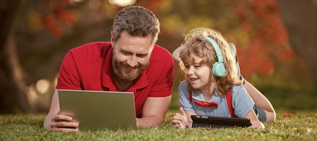 Banner of father on son school boy with laptop study online\
lying on grass webinar video lesson online education on laptop\
father and son use modern communication technology