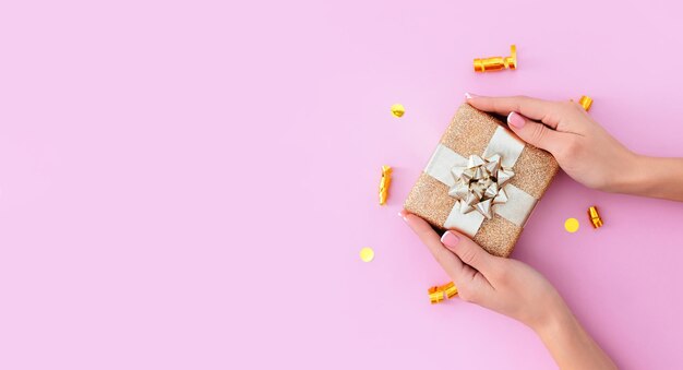 Banner gift box in female hands on a pastel pink background with place for text