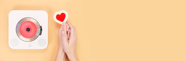 Photo banner of hands holding heart shape gift card next to white cd player with red disc on yellow