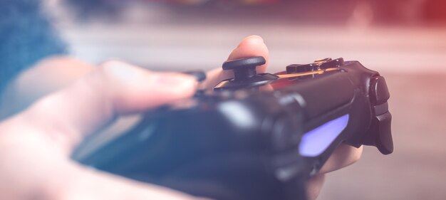 Banner hands with wireless controller for playing video games on a console at home, close-up view of joystick in neon lights