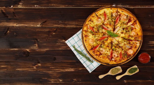 Banner di pizza di pesce fatta in casa con gamberi, bastoncini di granchio, peperoni su vassoio di legno, tavolo, decorato con salsa di pomodoro, ketchup, ingredienti di origano con tovagliolo in cucina e spazio copia.