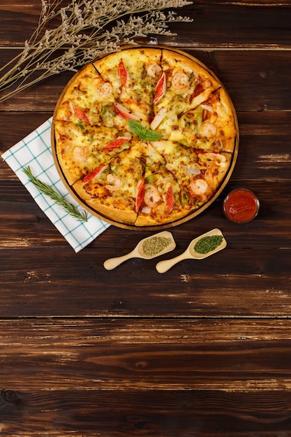 Banner of homemade seafood pizza with shrimp, crab sticks, bell peppers topping on wooden tray, table, decorated by tomato sauce, ketchup, oregano ingredients with napkin in kitchen and copy space.