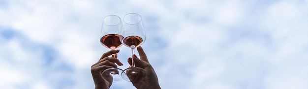 Banner image of the hands of a young female couple toasting with wine glasses