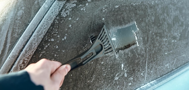 車の窓から氷を取り除くバナー画像大雪のセレクティブフォーカスの後、車から雪を取り除く