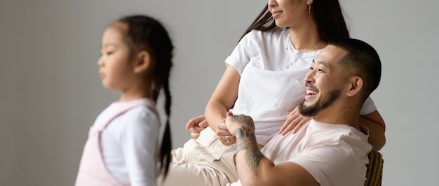 Foto immagine di banner di un giovane uomo asiatico sorridente che tiene la mano di sua moglie vicino a una bambina sfocata isolata