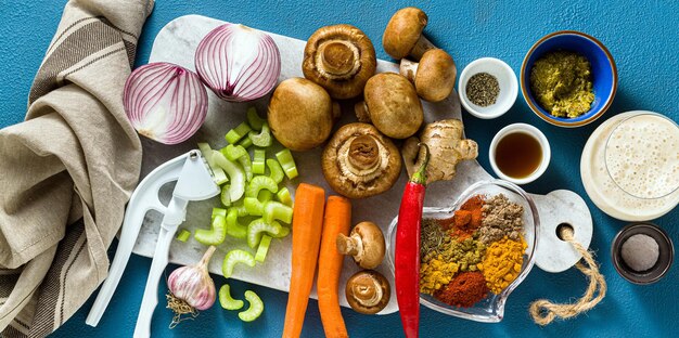 Banner di ingredienti per cucinare il curry indiano di verdure, zucche e funghi su sfondo blu e spezie riprese dall'alto dello spazio di copia