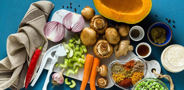 Banner of Ingredients for cooking Indian curry from vegetables pumpkins and mushrooms on a blue background and spices shot from above copy space