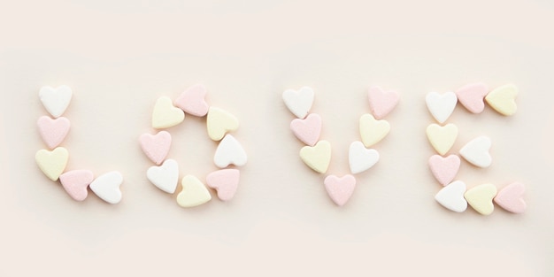 Banner inscription love with yellow pink and white candy hearts on a beige background.