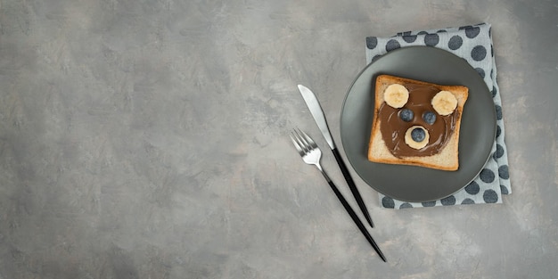 Баннер детского завтрака или обеда или закусочного тоста с шоколадной пастой из фундука, бананом и черникой в форме милого медведя. Меню детского питания