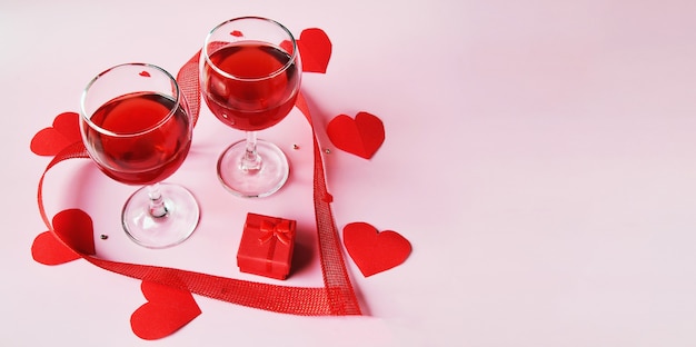 Banner on a light surface two glasses of red wine, a red gift box with red hearts and a ribbon