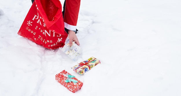 Banner man verkleed als Santa Claus verzamelt geschenken in een besneeuwd bos in de sneeuw kleurrijke dozen met geschenken