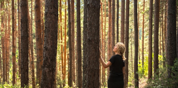 banner met volwassen vrouw in zonnig dennenbos idee van het herstellen van gezondheid en ontspanning bosbaden