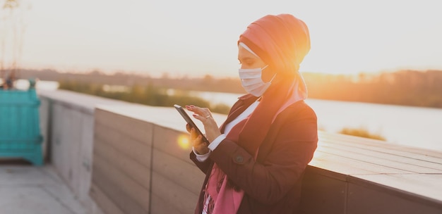 Banner Moslimvrouw in hijab houdt smartphone vast met internet buiten Arabische vrouw draagt medisch masker terwijl ze ziek is