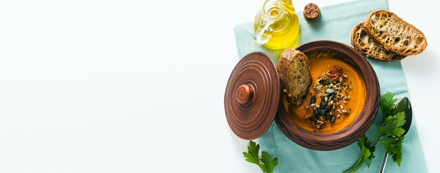 Banner di zuppa di zucca con semi e pane di segale fresco in una ciotola di argilla su un tavolo