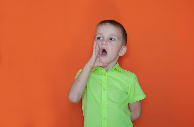 Banner sale discount win winner\'s concept a charming happy boy\
looks into the camera with his mouth open and screams against an\
orange background advertising of a children\'s store